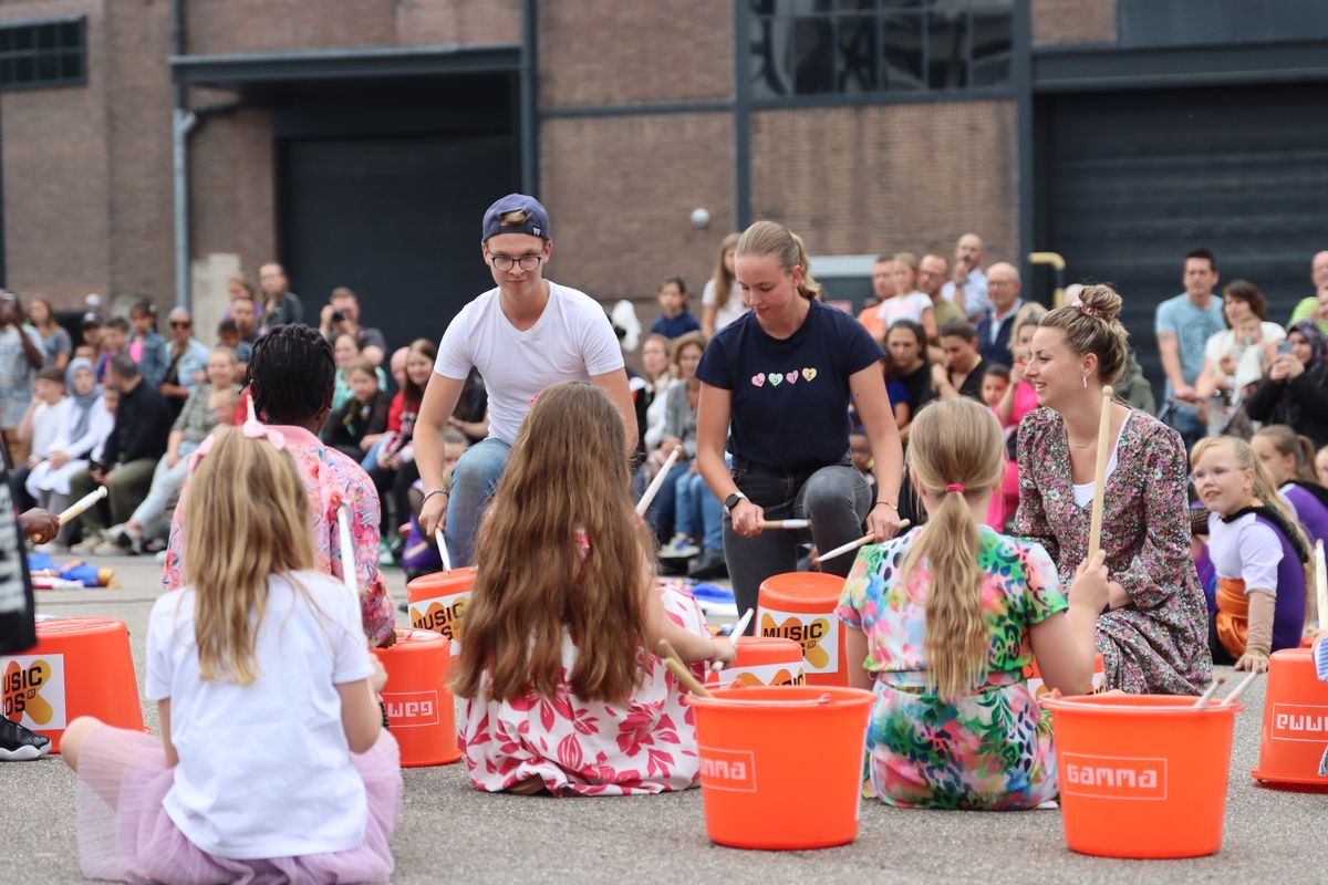 Kinderen trommelen op emmers tijdens een optreden van Music Kids